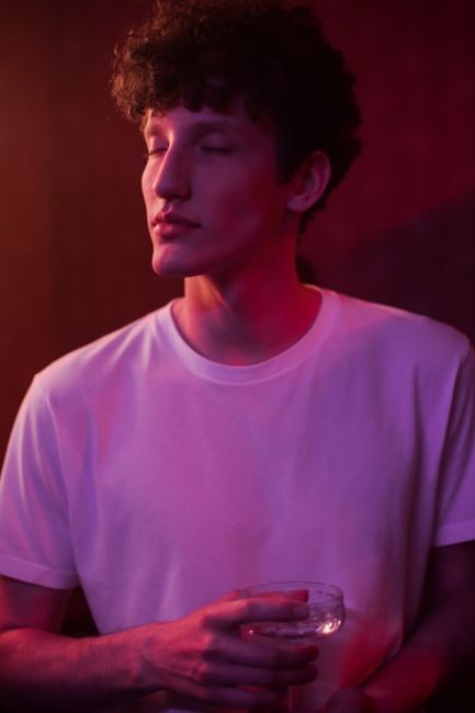 Young man in a white t-shirt enjoying a drink at a neon-lit party.