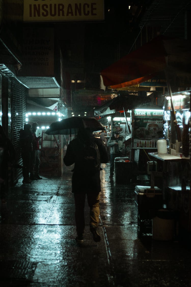 Unrecognizable Person Walking On Street With Umbrella At Night