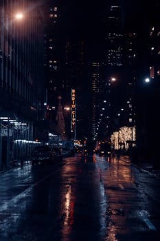 Empty wet asphalt road between modern skyscrapers in rainy New York City at night