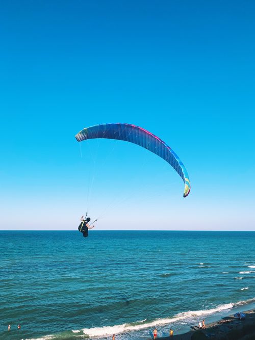 Free Back view of anonymous person flying on paraglider near waving ocean and beach on summer sunny day Stock Photo