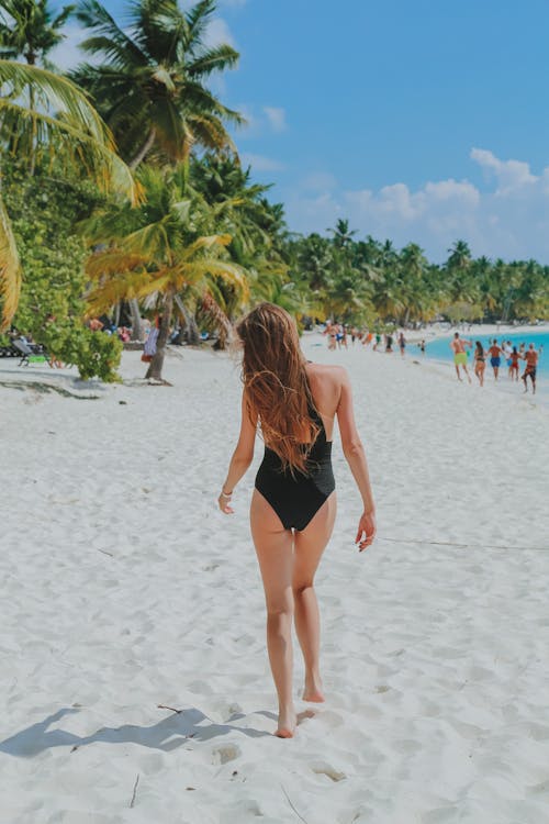 Faceless female tourist in swimwear walking on sandy beach