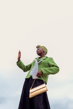 From below of fashionable young African American female in trendy outfit and stylish turban against cloudy sky