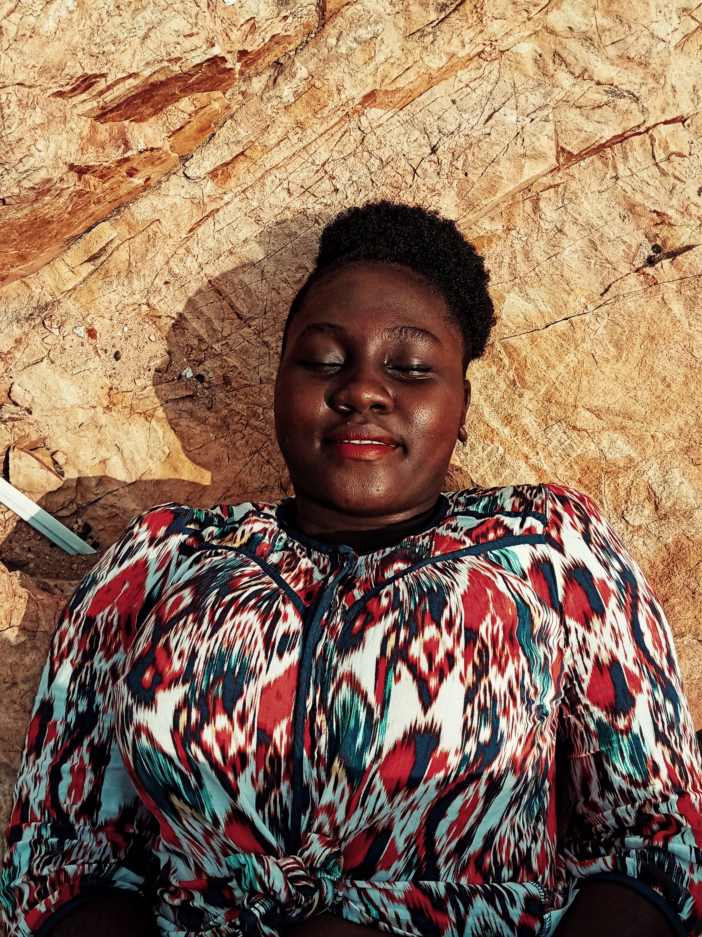 From above of positive plus size African American female with afro hairstyle wearing colorful shirt and lying on stony surface with eyes closed