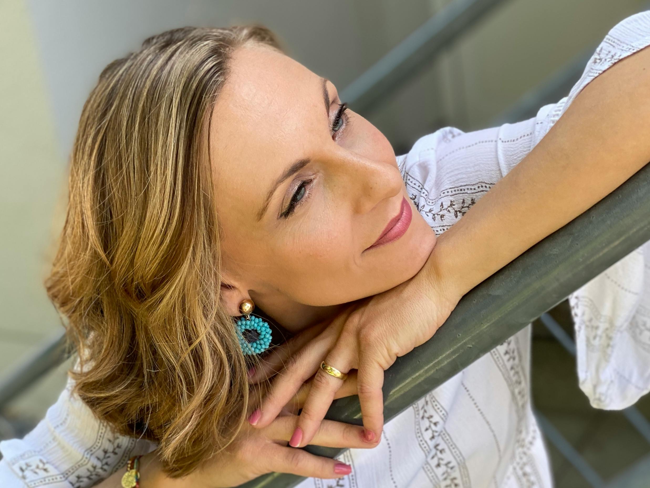 Close-up portrait of a woman leaning against a railing, smiling softly outdoors.
