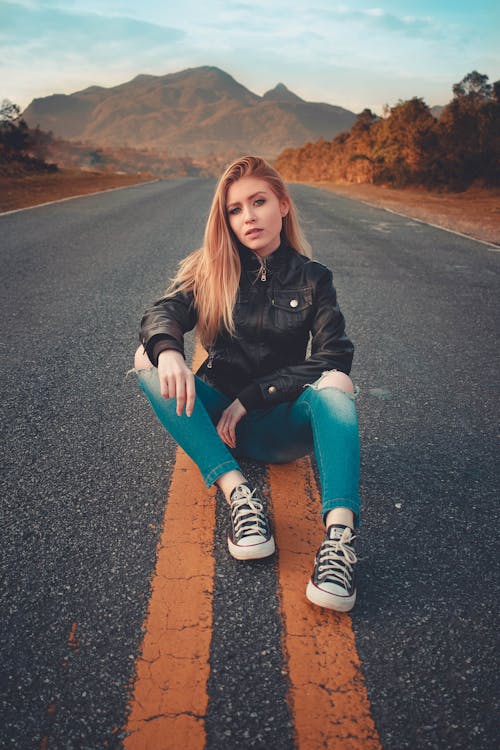 Woman in Black Jacket and Blue Jeans Sitting on Road