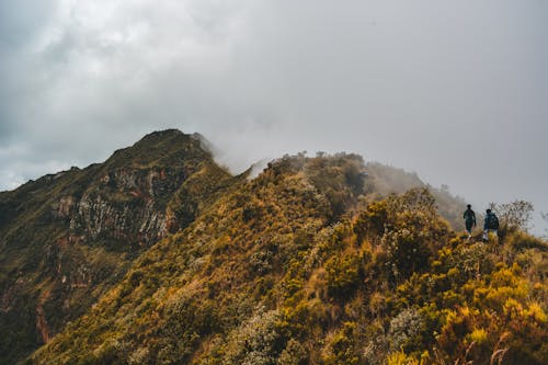 People Hiking on Green and Brown Mountain Under White Clouds
