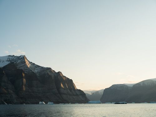 Free Peaceful coastal view featuring snow-covered mountains and calm waters at twilight. Stock Photo