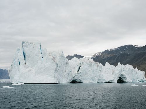 Free A colossal iceberg floating in the frigid ocean with majestic mountains in the distance. Stock Photo