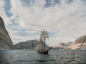 Brown Boat on Sea Near Brown Mountains Under Gray Clouds