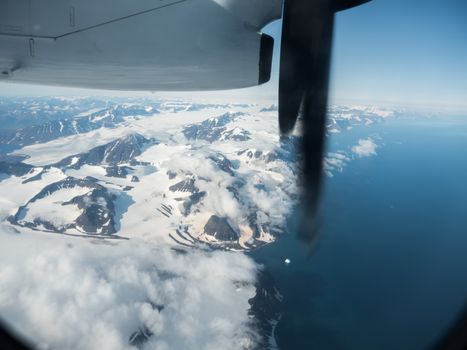 Scenic aerial view from an airplane window of snow-covered mountains and ocean under a clear sky.