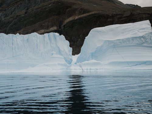 Free A stunning iceberg floating in serene Arctic waters against a rocky mountain backdrop. Stock Photo