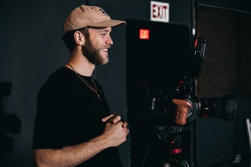 Free Smiling cameraman on film set operating video camera, showcasing behind-the-scenes filmmaking. Stock Photo