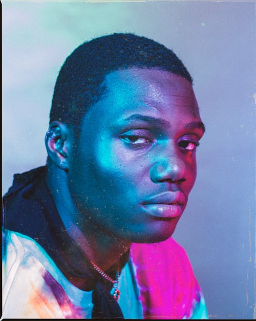 Free Confident African American man with black hair in trendy clothes illuminated by multicolored neon lights and looking at camera Stock Photo