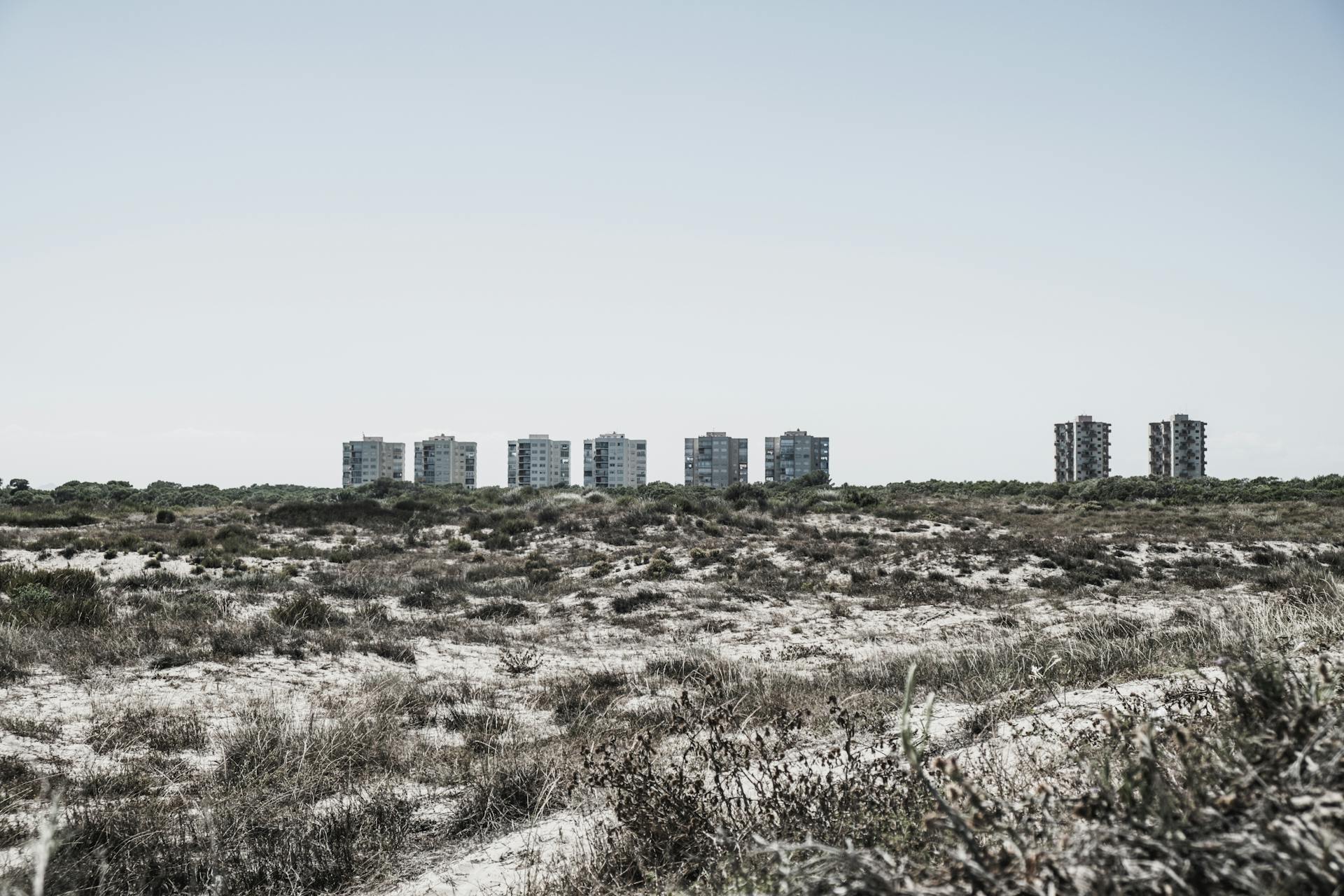 Brutalist buildings line the horizon in Valencia, Spain, over a sandy, natural terrain.