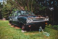 Rusty automobile with tow rope without wheels and with no hood placed on grassy terrain near tree in daylight in nature