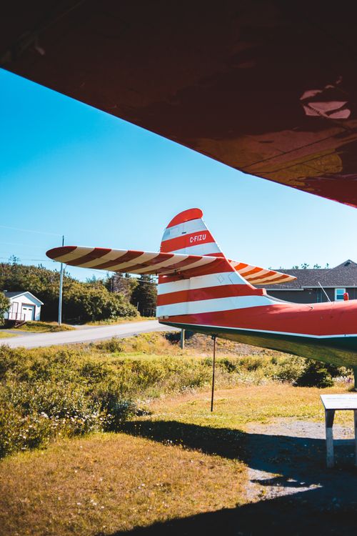 Free Red and white tail of rescue aircraft parked in hangar near grassy field in countryside against cloudless blue sky Stock Photo