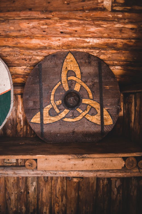 Aged wooden Viking shield decorated with ornament placed on lumber shelf in traditional museum in Norstead village