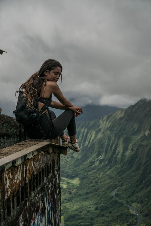 Free Back view of slim traveler with backpack resting on shabby rough brick roof above mountains under foggy sky Stock Photo