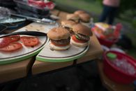 Tasty fresh baked burgers with cucumber served on plate on table near food and different products