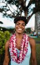 Cheerful African American female in traditional leis flower garland and big earrings in local green yard with bushes and trees