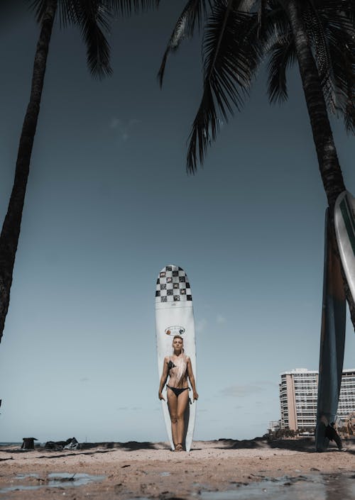 Graceful woman standing near surfboard on sandy beach