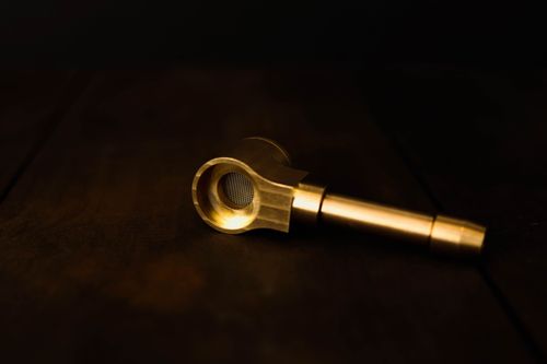 Free Close-up of a golden metal pipe on a dark wooden surface, showcasing intricate craftsmanship. Stock Photo