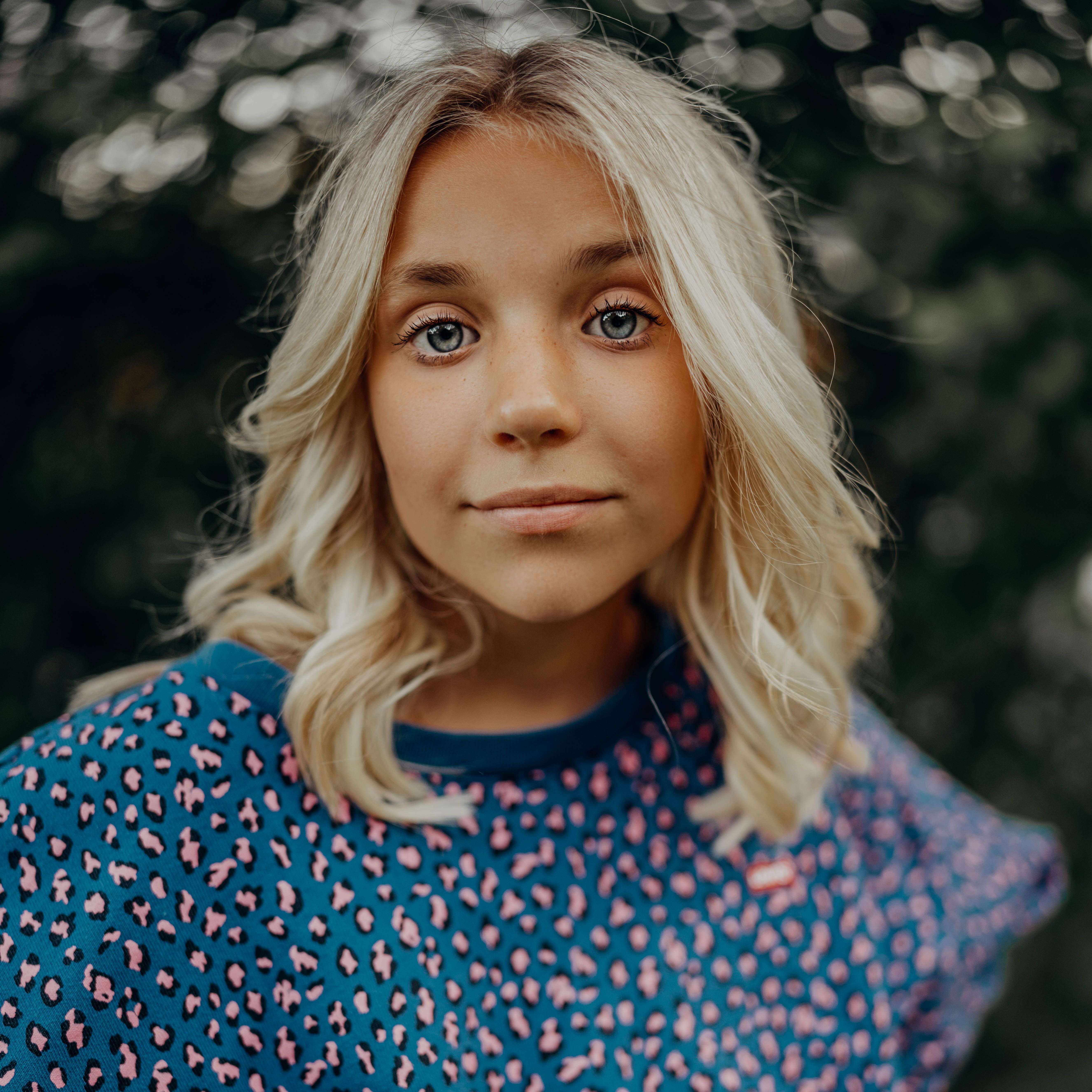 Close-up portrait of a young blonde woman outdoors in a blue patterned sweater.