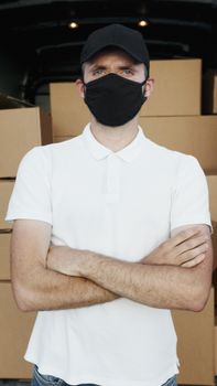 A courier in a white polo shirt, black mask, and hat standing with packages.
