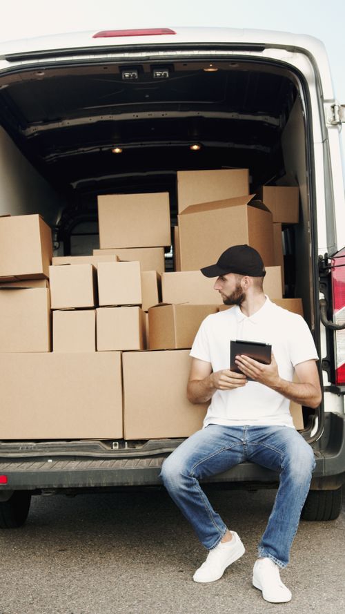 A courier checking a tablet beside parcels in a van