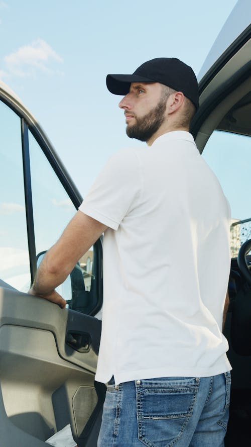 Man in White Crew Neck T-shirt Standing Beside the Vehicle