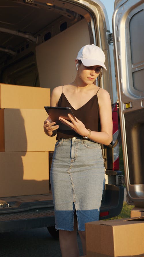Woman in Black Tank Top and Denim Skirt Looking at Boxes