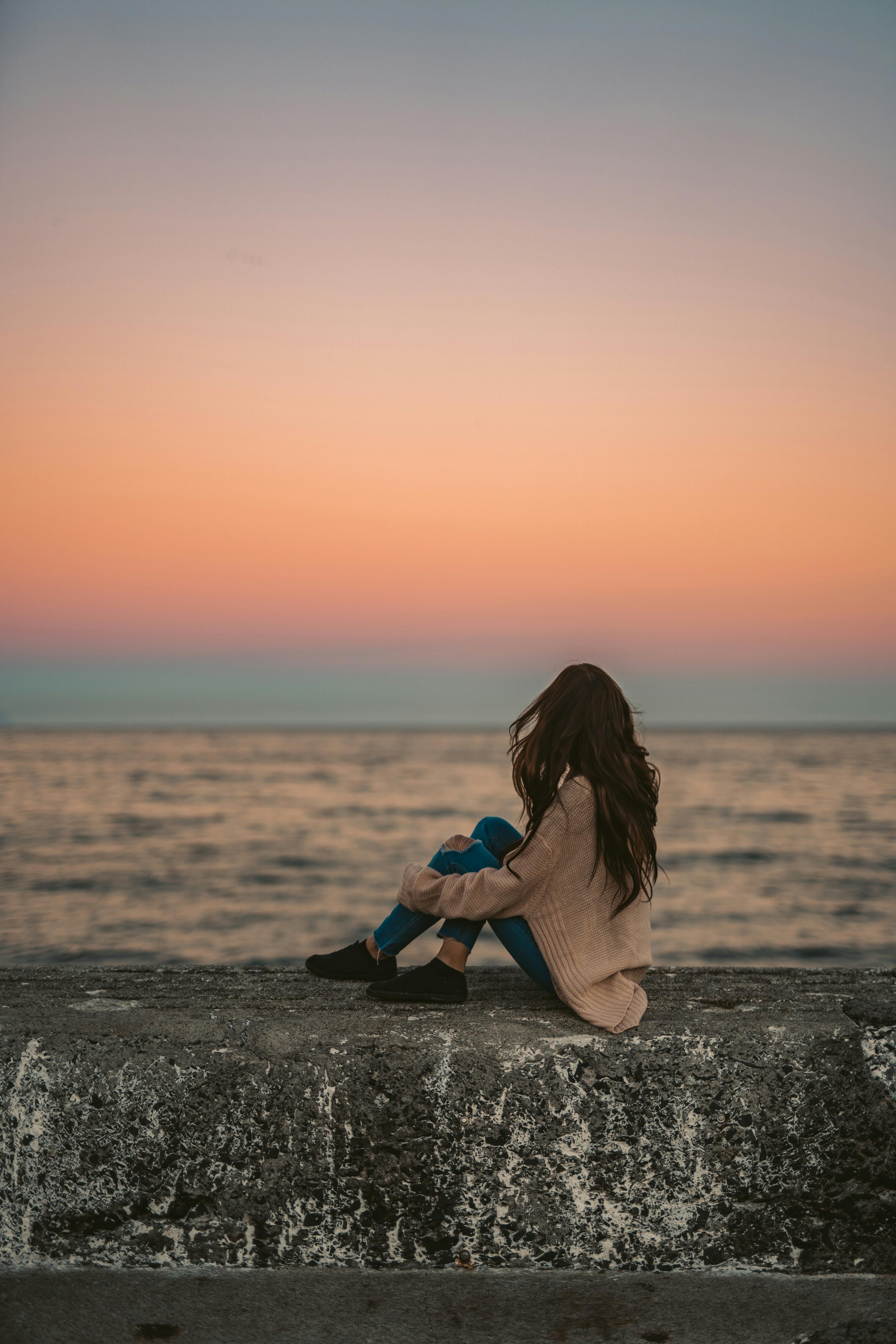 一名妇女坐在开普敦的防浪堤上，享受着海上宁静的日落