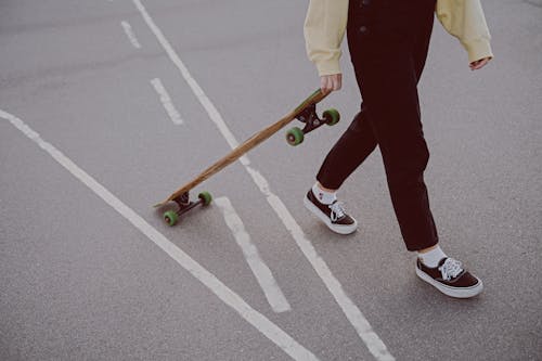 Photo of a Person in Black Pants Walking while Holding a Longboard