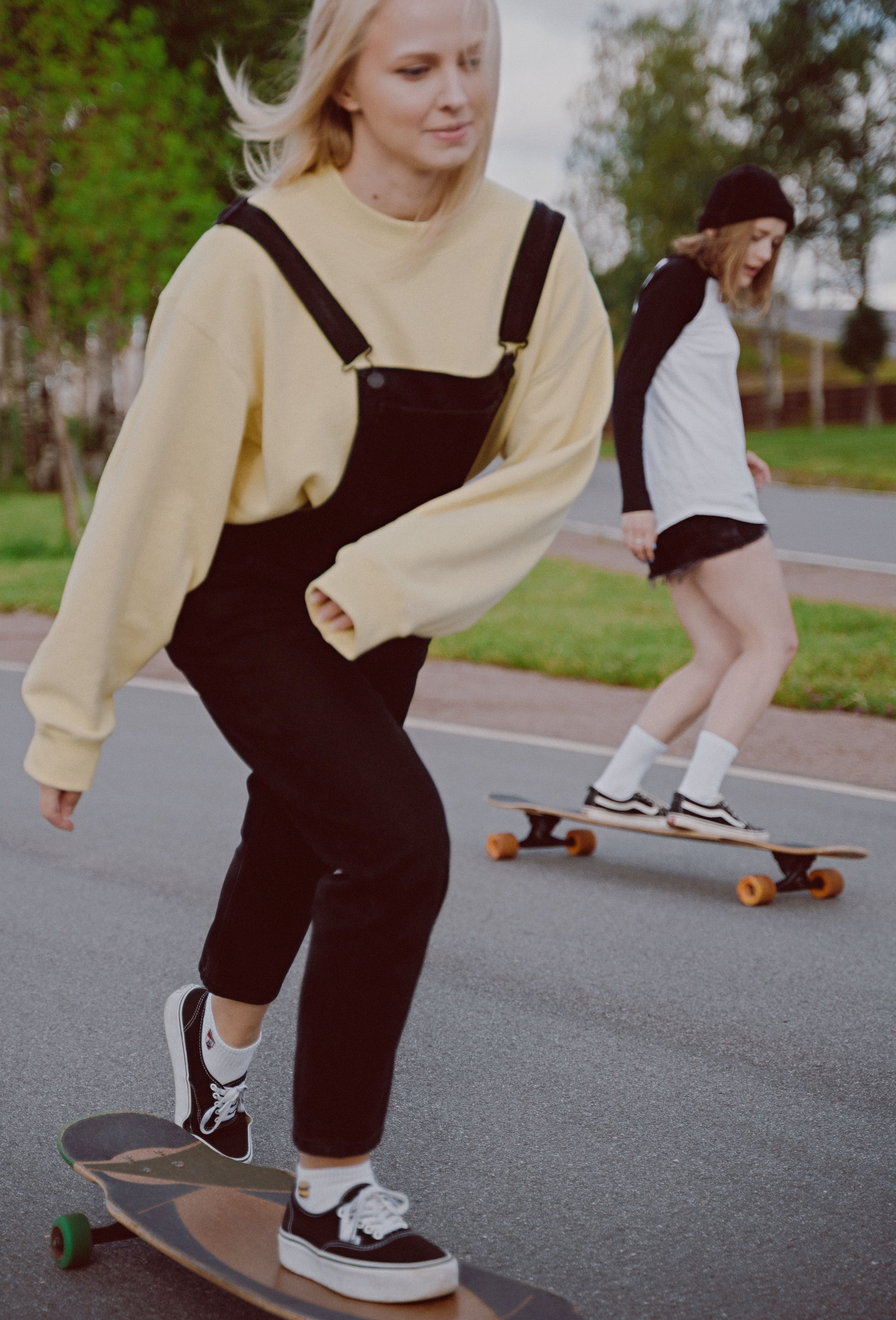 两名女子穿着街头服饰，在公园里悠闲地骑长板度过一天