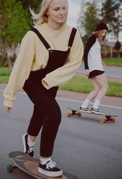 两名女子穿着街头服饰，在公园里悠闲地骑长板度过一天