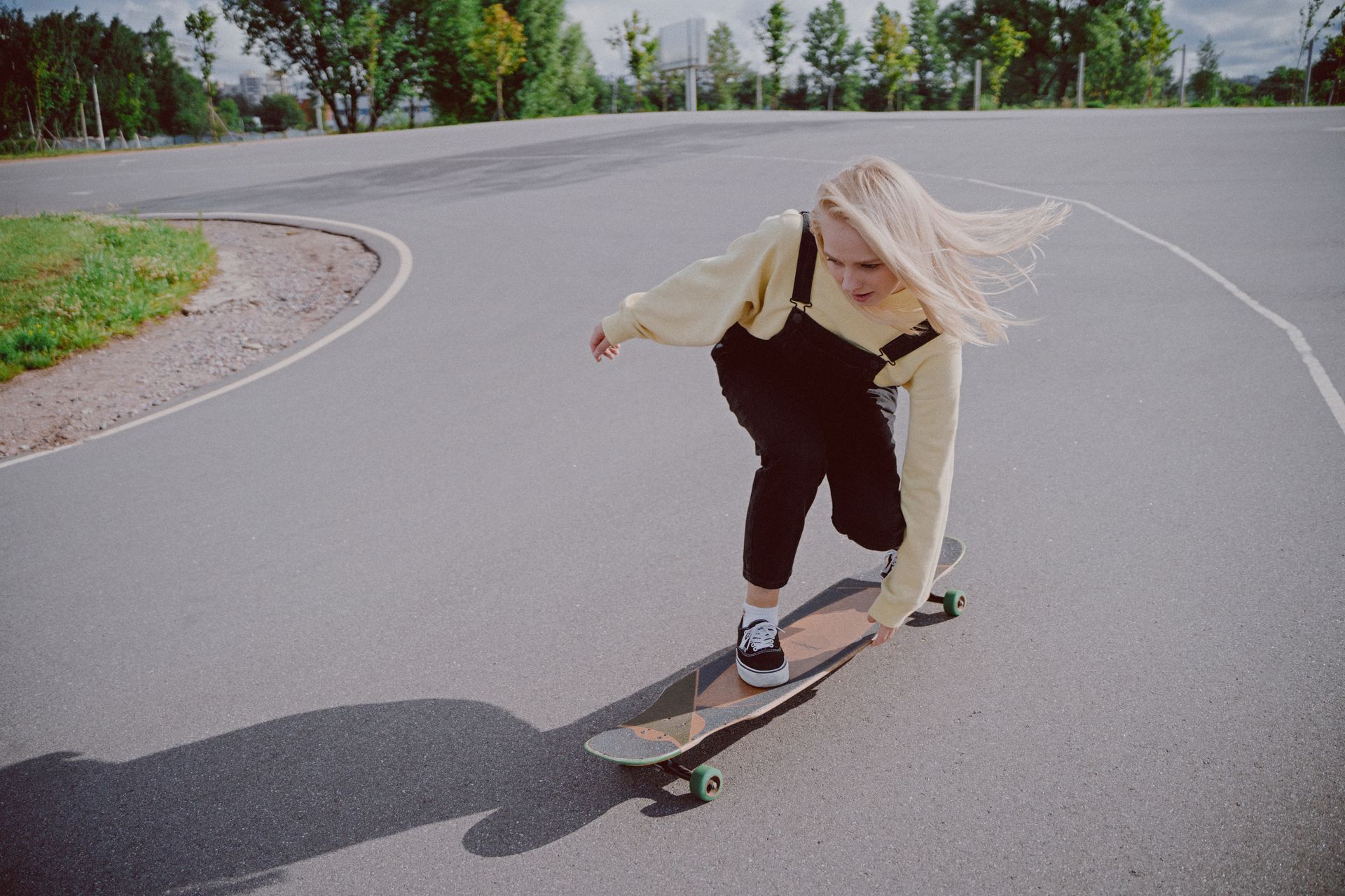 Blonde woman skateboarding on a longboard outdoors, showcasing balance and skill on an empty road.