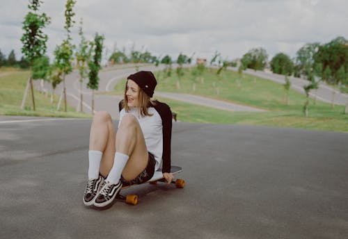 Woman in White and Black Top and Black Shorts Sitting on a Longboard