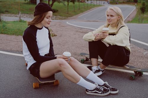 Free Two women relaxing outdoors, enjoying coffee and conversation with skateboards. Stock Photo
