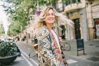 一位金发女子面带微笑，身穿时尚外套，头发在城市街道上飘扬的肖像