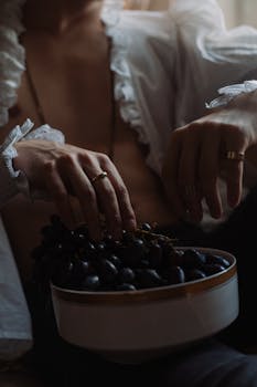 A moody portrait showcasing hands delicately holding a bowl of grapes, set against a dark background.