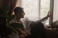 一位身着白衬衫、神情专注的男人凝视着敞开的窗户，显得优雅而内省