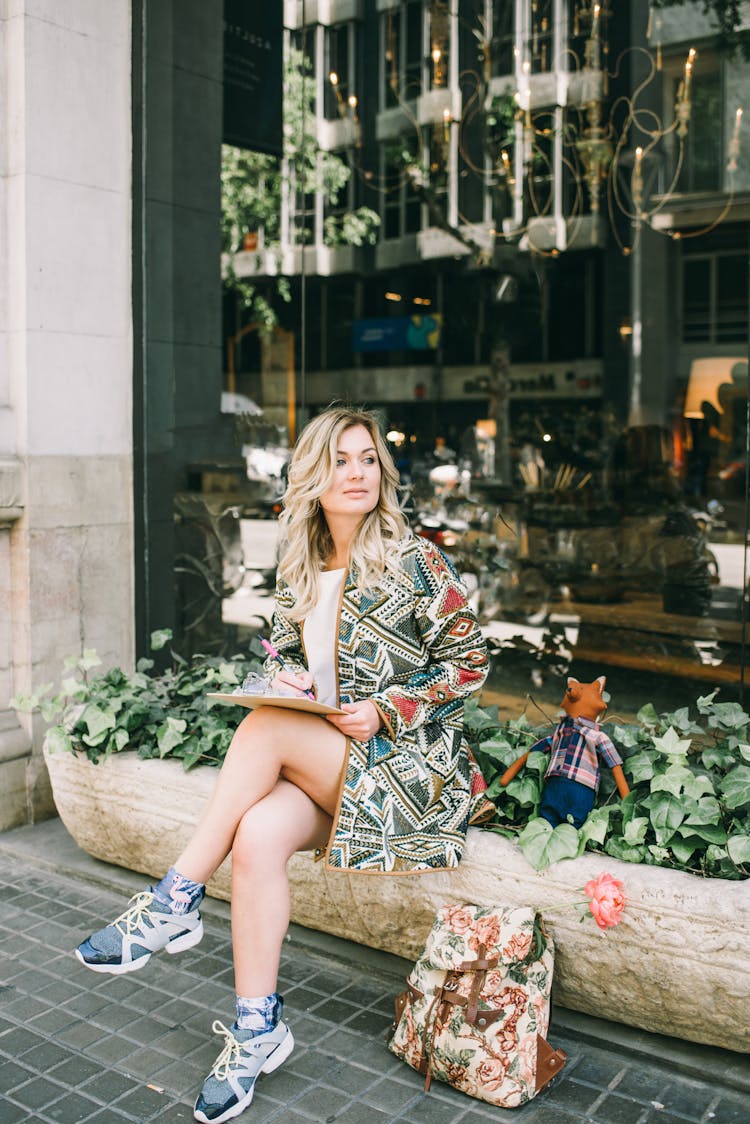 Woman In Printed Jacket Sitting On A Plant Box