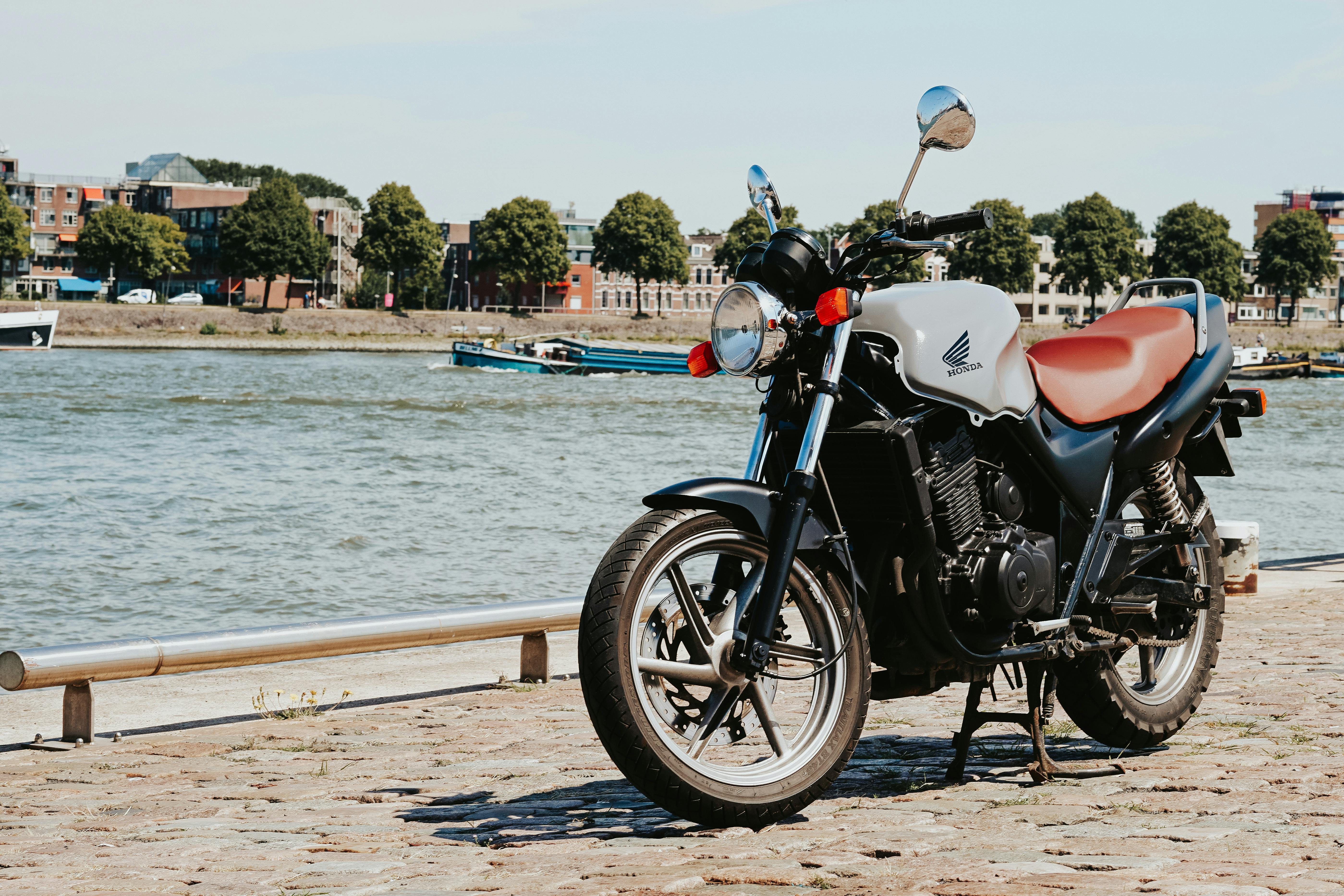 A vintage Honda motorcycle parked by a scenic riverside on a sunny day.