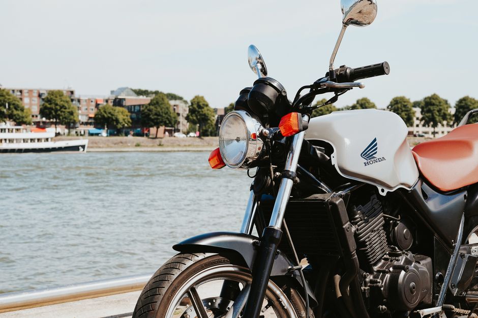Close-up of a Honda motorcycle parked by a river on a sunny day, with urban background.