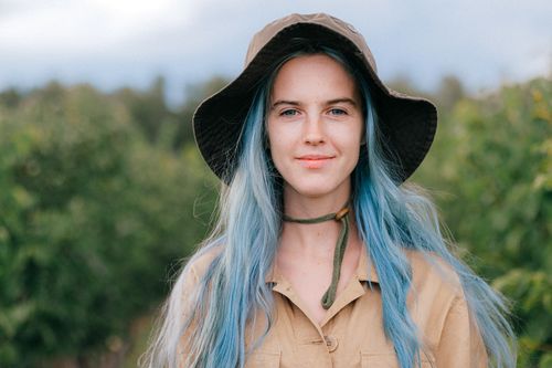 Free A young woman with blue hair smiles gently, wearing a hat in an outdoor setting. Stock Photo