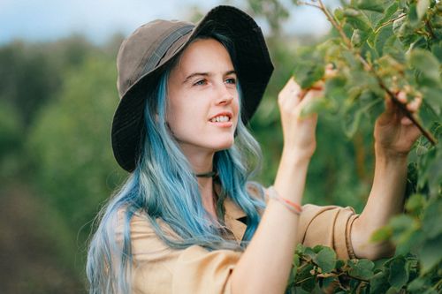 Free A young woman with blue hair and a hat picking plants outdoors during the day. Stock Photo