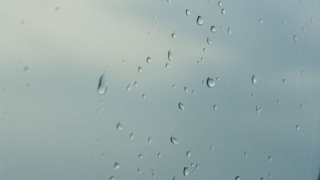 雨滴在玻璃窗上留下特写，背景是多云的天空，营造出一种宁静而平静的氛围