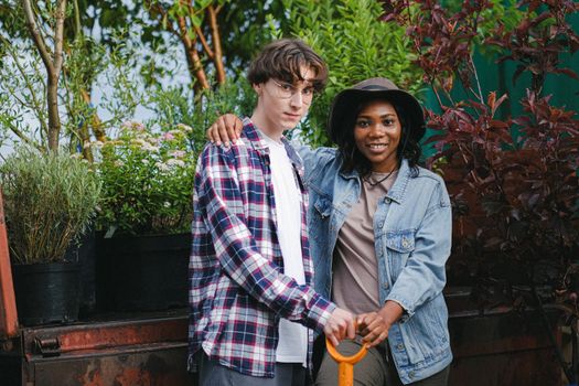 A diverse couple posing together with gardening tools amidst lush plants.