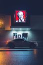 Dark car on paved roadway at window of drive thru cafe under glowing sign late at night