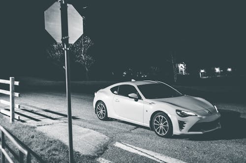 Free Black and white sport grand tourer car on asphalt roadway near road sign at night Stock Photo